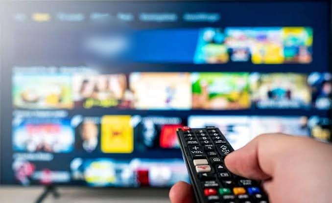 Hand holding a TV remote in front of a television showing a streaming menu